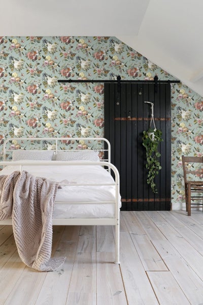 Helles Schlafzimmer mit Blumentapete, weißem Metallbett, schwarzer Schiebetür und hellem Holzboden.