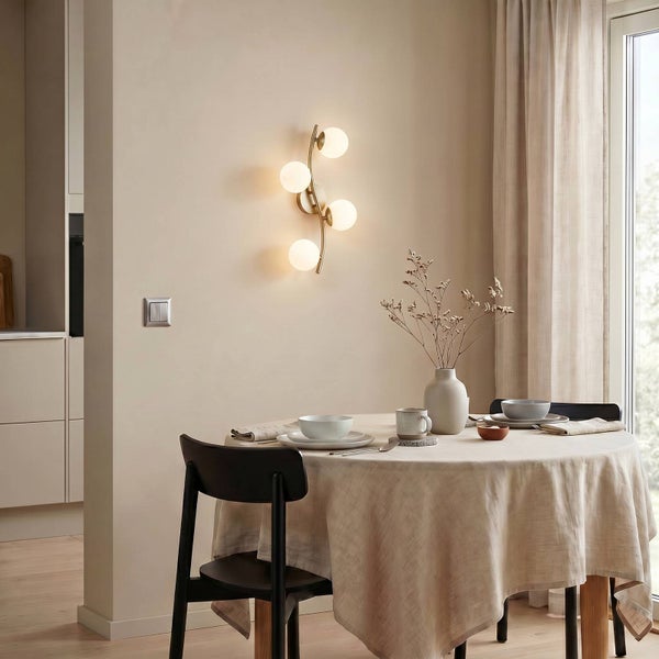 Moderne Wandleuchte mit vier runden Glasschirmen über einem gedeckten Esstisch in einem hellen, minimalistischen Esszimmer.