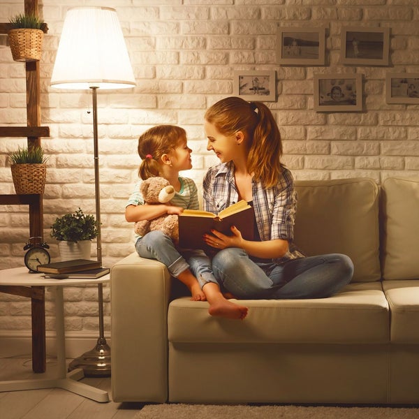 Wohnzimmer mit hellem Sofa vor einer weißen Ziegelwand und einer Stehlampe. Eine Frau und ein Kind lesen in gemütlicher Atmosphäre.
