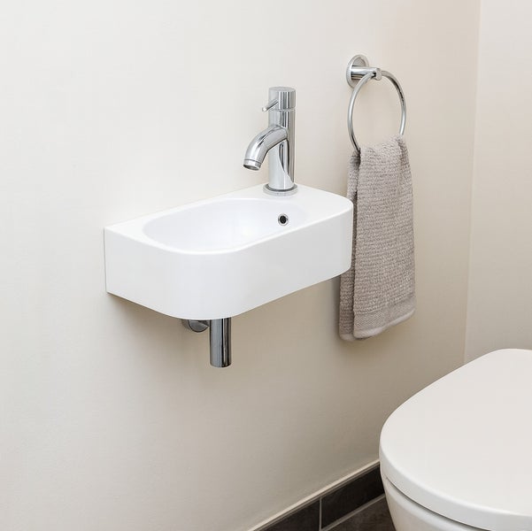 Kompaktes Wand-Handwaschbecken in einem hellen Gäste-WC mit verchromter Armatur und Handtuchring.