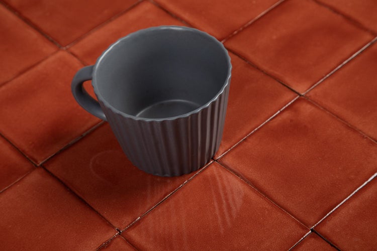 Graue Tasse auf braunen Fliesen