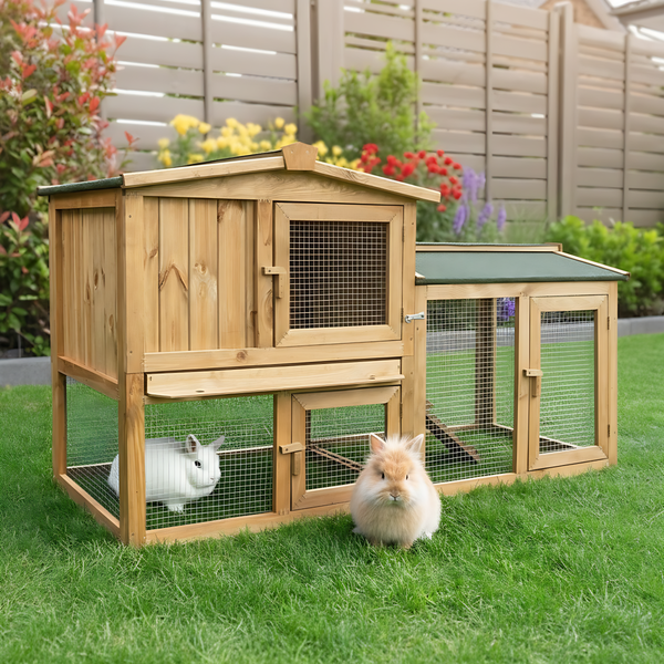 Zweistöckiger Kleintierstall aus Holz mit Freilaufgehege auf einer Rasenfläche in einem hellen Garten.