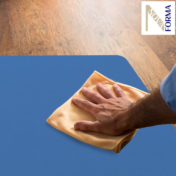 Eine Hand reinigt eine Bodenschutzmatte mit einem Tuch auf einem Holzfußboden. NOVA FORMA Logo.