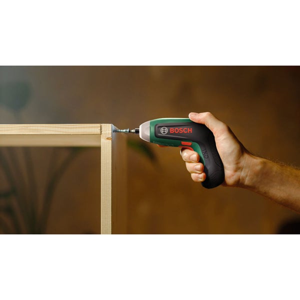 Eine Hand hält einen Bosch IXO Akkuschrauber und schraubt eine Schraube in eine Holzplatte für den Möbelbau.