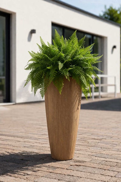 Hoher Pflanzkübel in Holzoptik mit Farn auf einer gepflasterten Terrasse vor einem modernen Haus.