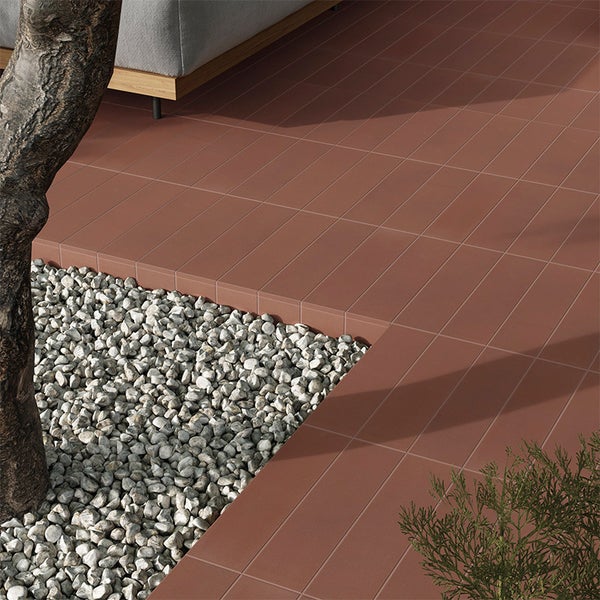 Terrasse mit rechteckigen Bodenfliesen in Terrakotta Optik und angrenzendem Kiesbeet im Garten.