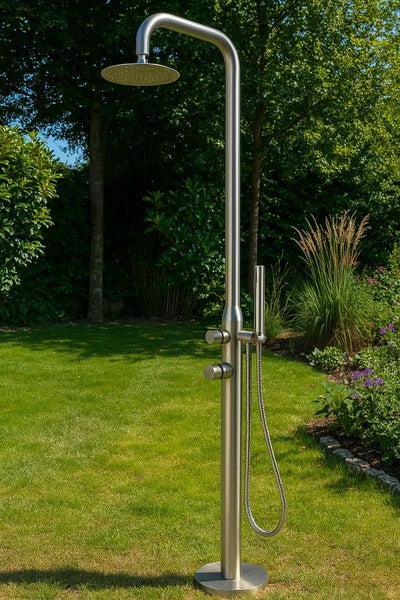 Freistehende Gartendusche aus Edelstahl mit großem Regenbrausekopf und separater Handbrause auf einer Rasenfläche in einem Garten.