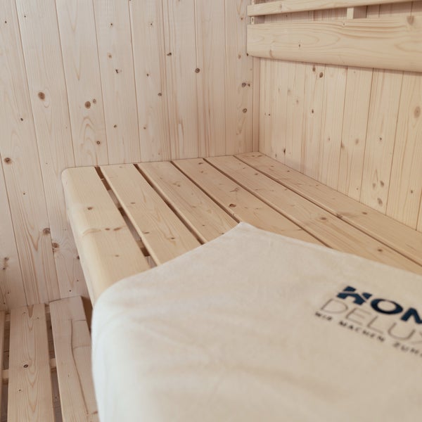 Saunabank aus hellem Holz mit einem Handtuch von Home Deluxe Logo in einer Sauna aus Kiefernholz.