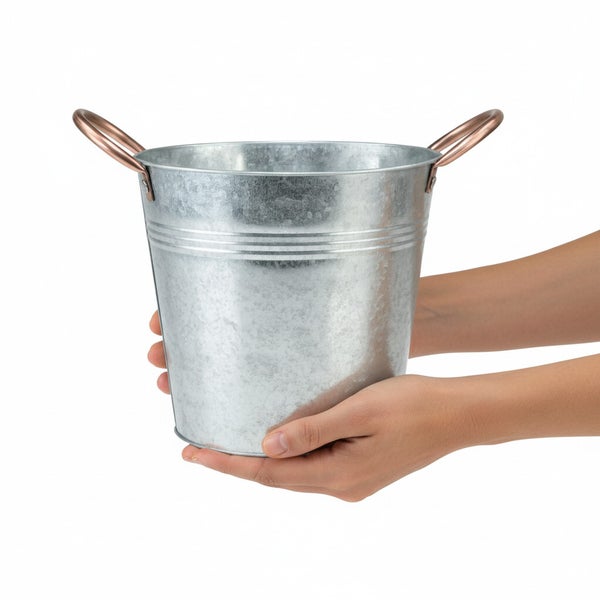 Ein verzinkter Metalleimer mit zwei Griffen wird in den Händen gehalten.