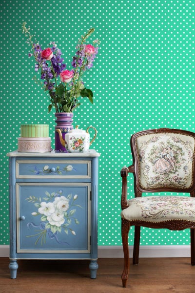 Dekoratives Zimmer mit blauem Beistelltisch, Blumen und Stuhl vor gepunkteter Tapete.