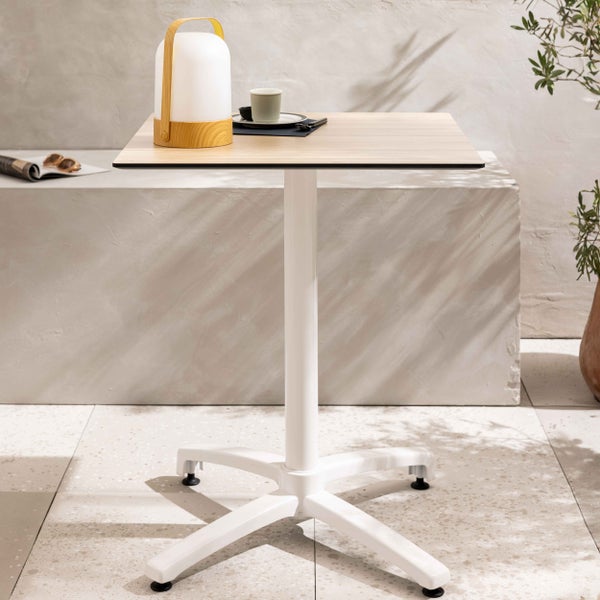 Moderner Bistrotisch mit quadratischer Tischplatte in Holzoptik und weißem Säulengestell auf einem hellen Boden im Außenbereich.