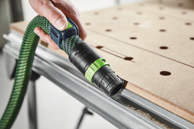 Eine Hand hält eine Festool Cleantec Anschlussmuffe mit Saugschlauch an einer Werkbank.