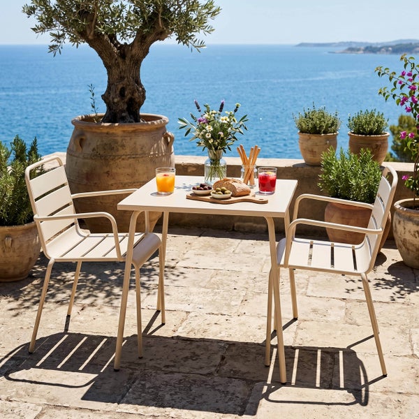 Modernes Gartenmöbel-Set aus Metall auf einer Steinterrasse mit Meerblick, bestehend aus einem quadratischen Tisch und zwei Stühlen.