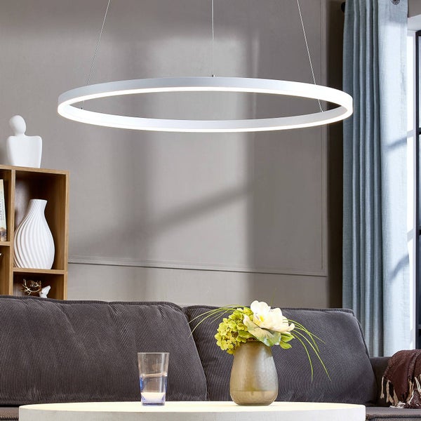 Moderne ringförmige LED-Pendelleuchte in einem hellen Wohnzimmer über einem grauen Cordsofa und einem Couchtisch mit Blumen.