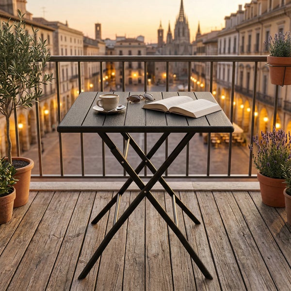 Balkonset aus schwarzem Metall mit Klapptisch und zwei Stühlen auf einer hellen Steinterrasse mit Stadtblick bei Abenddämmerung.