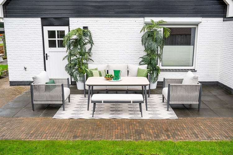 Moderne Garten-Lounge-Gruppe auf einer Terrasse mit Sofa, Sesseln, Bank und Tisch, Seilbespannung und hellen Polstern.