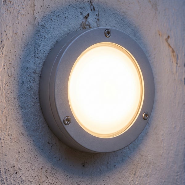 Runde LED Außenwandleuchte mit mattem Gehäuse, montiert an einer hellen Putzfassade.