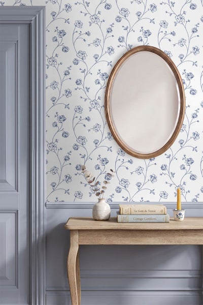 Klassische Blumentapete mit blauem Rankenmuster auf weißem Hintergrund, kombiniert mit einem ovalen Spiegel und einem Holztisch im Landhausstil.