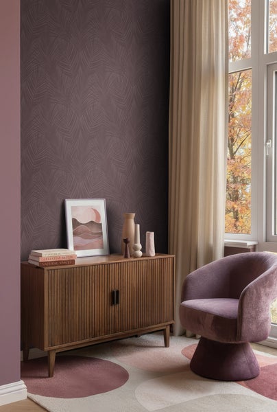 Modernes Zimmer mit dunkellila Tapete mit Palmblattmuster, einem Sideboard aus Holz, einem Polstersessel und Vorhängen am Fenster.