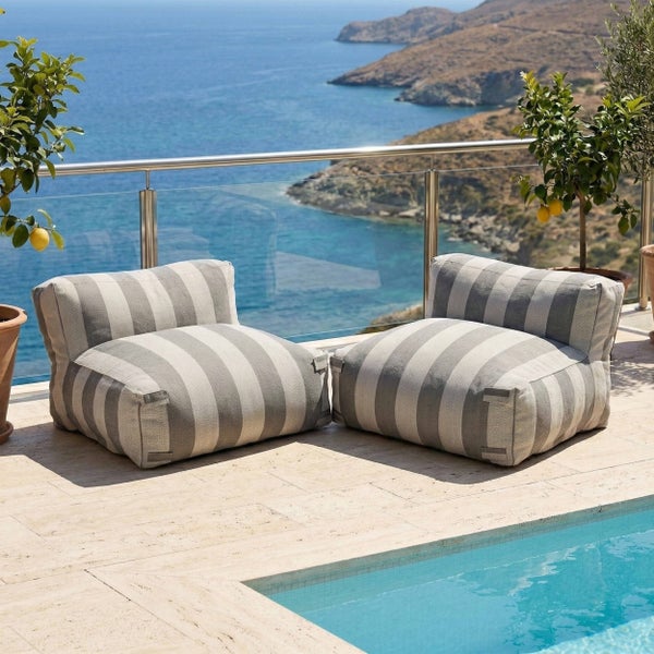 Zwei grau-weiß gestreifte Outdoor-Lounge-Sessel auf einer hellen Steinterrasse am Pool mit Meerblick und Zitronenbäumen.