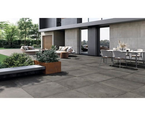Moderne Terrasse mit grossformatigen dunkelgrauen Feinsteinzeugfliesen, kombiniert mit Sitzbereichen und Lounge-Möbeln in einem Garten.