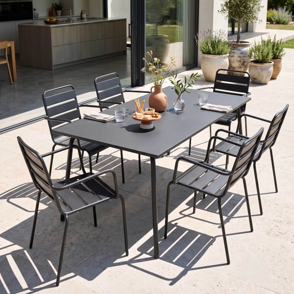 Modernes Gartenmöbel-Set aus Metall mit einem rechteckigen Esstisch und sechs Armlehnenstühlen auf einer hellen Terrasse vor einer Glasfront.
