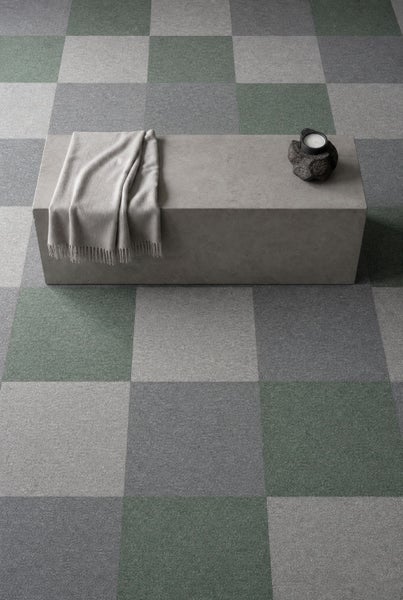 Teppichfliesen im Schachbrettmuster in Grün- und Grautönen in einem modernen Raum mit Betonbank, Decke und Kerze.