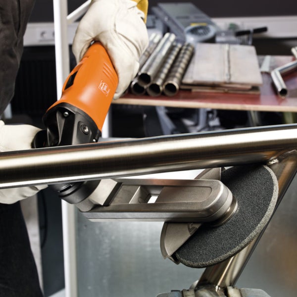 Person mit Schutzhandschuhen bearbeitet ein Edelstahlrohr mit einem Kehlnahtschleifer in einer Werkstatt. Fein Logo.