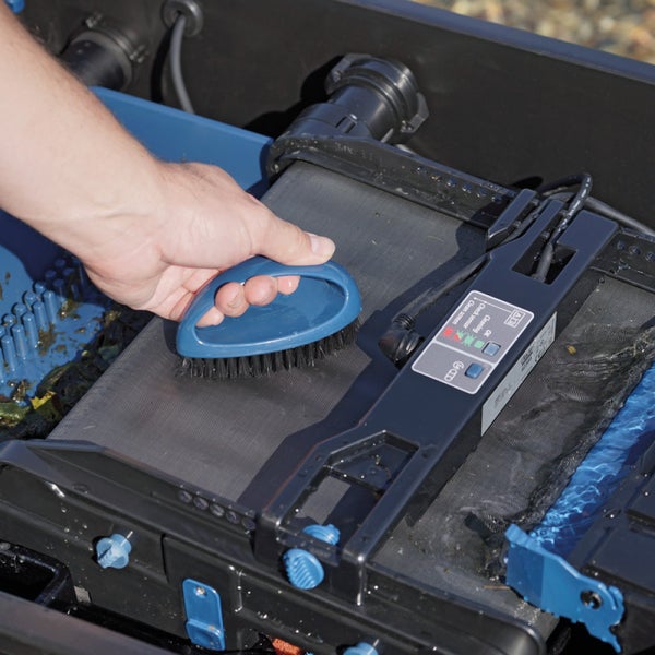 Hand reinigt das Sieb eines Teichfilters mit einer Bürste.