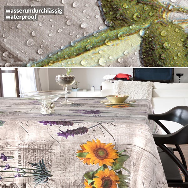 Wasserundurchlässige Tischdecke mit Sonnenblumen- und Lavendelmuster in einem hellen Zimmer. Detailansicht zeigt Wassertropfen auf der Oberfläche.