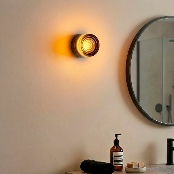 Moderne runde Wandleuchte mit warmem Lichteffekt in einem Badezimmer mit Spiegel und Accessoires.