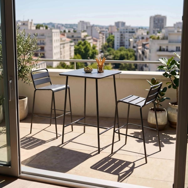 Moderner Balkon-Stehtisch mit zwei Barstühlen aus Metall auf einem hellen Balkon mit Pflanzen und Stadtblick.