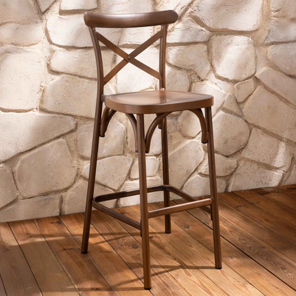 Barhocker aus Holz mit Kreuzlehne und Fußstütze, rustikaler Stil, auf Holzboden vor einer Steinwand.