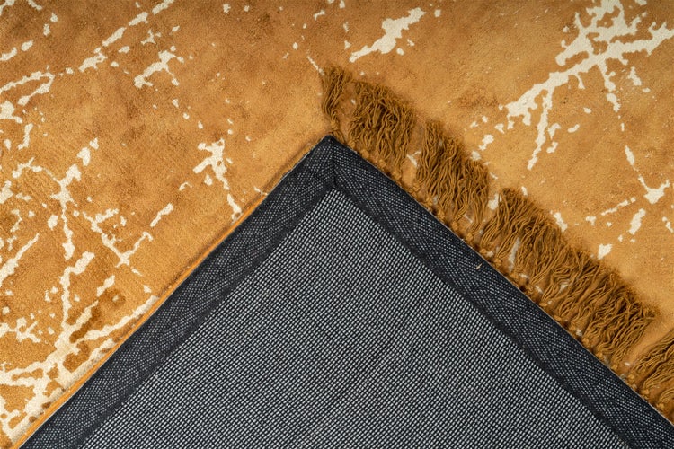 Detailansicht eines Teppichs mit abstraktem Muster und Fransen, die rutschfeste Rückseite ist an einer umgeklappten Ecke sichtbar.