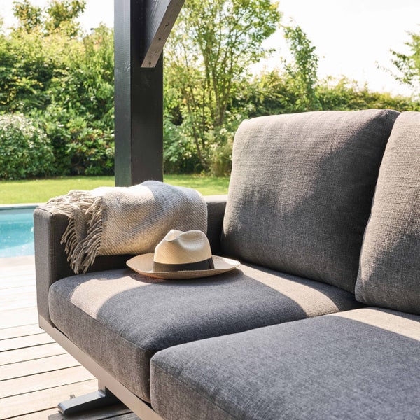Graues Outdoor-Loungesofa mit Stoffpolstern auf einer Holzterrasse neben einem Pool im sonnigen Garten.