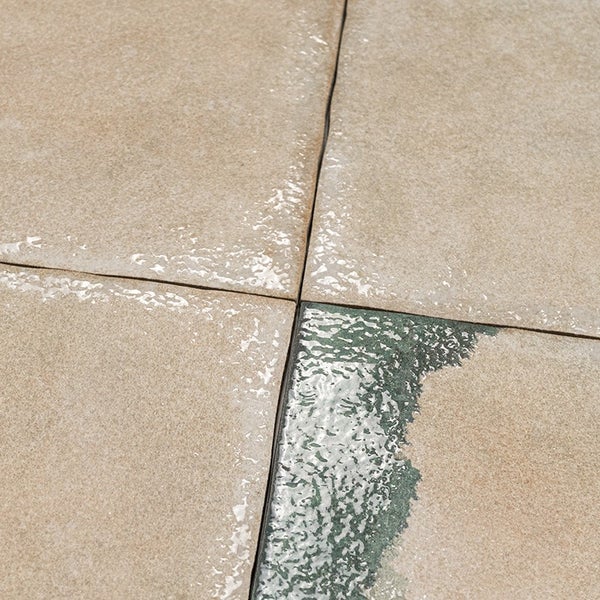 Draufsicht auf vier quadratische Terrassenplatten mit einer texturierten Oberfläche und Feuchtigkeitsspuren in den Fugen.