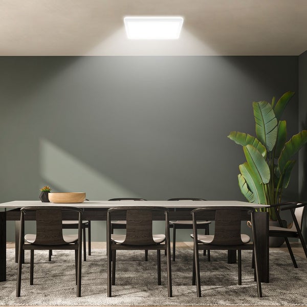 Quadratisches LED-Panel an der Decke beleuchtet ein modernes Esszimmer mit Holztisch, dunklen Stühlen und einer großen Zimmerpflanze.