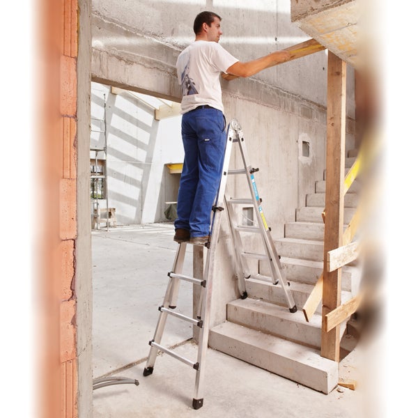 Mann misst Höhe mit einem Zollstock auf einer Mehrzweckleiter in einem Rohbau