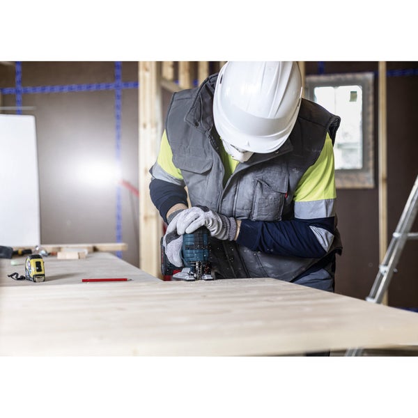 Ein Handwerker mit Schutzhelm verwendet eine Stichsäge auf einer Holzplatte.