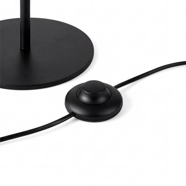 Detailaufnahme eines runden schwarzen Lampenfußes mit einem runden schwarzen Trittschalter am Kabel.