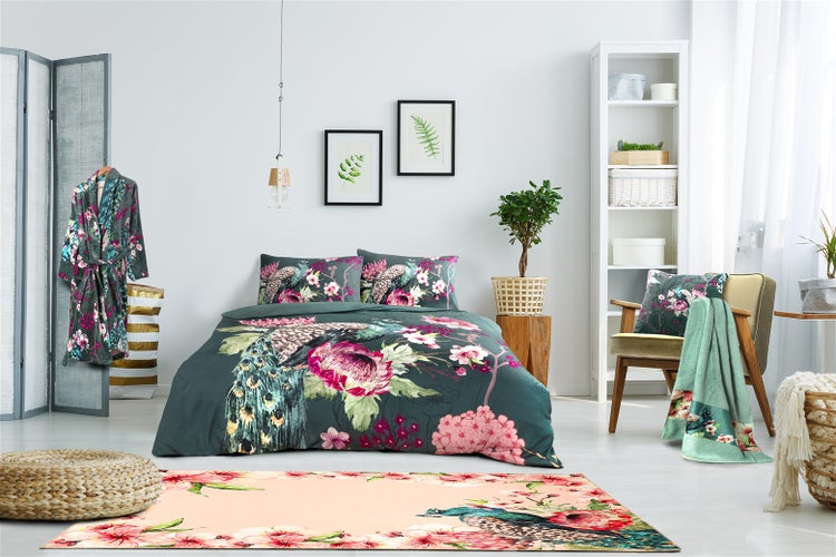 Ein helles Schlafzimmer mit einem Doppelbett, das mit einer Bettwäsche mit Pfauen- und Blumenmotiv ausgestattet ist, sowie einem passenden Teppich.