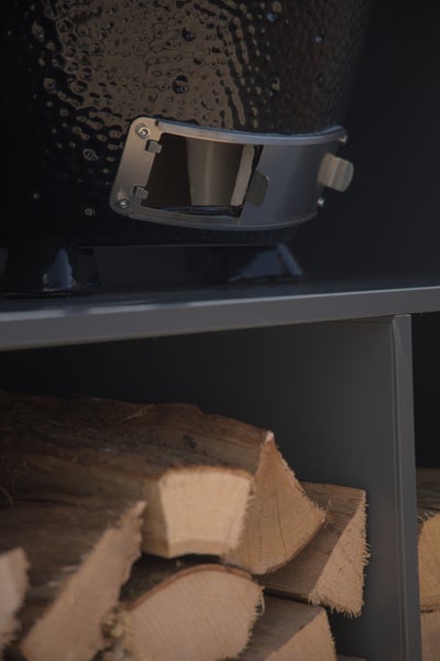 Detailansicht eines Holzkohlegrills mit Holzregal und Brennholz