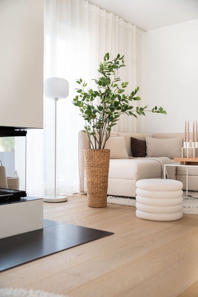 Helles Wohnzimmer mit Parkettboden, beigem Sofa, großer Zimmerpflanze in einem Pflanzkorb und weißer Stehlampe.