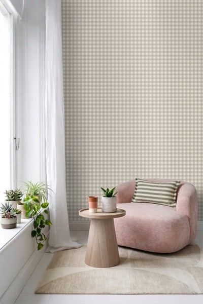 Vliestapete mit Karomuster in Beige und Weiß in einem hellen Wohnzimmer mit rosa Sessel, Holzbeistelltisch und Zimmerpflanzen am Fenster.