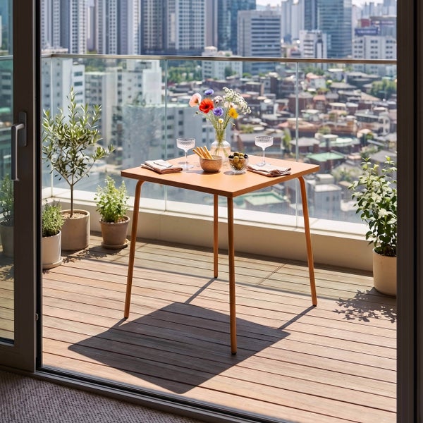 Moderner Balkon mit Holzterrasse, Glasgeländer und Pflanzen. Quadratischer Metalltisch mit Blumen und Snacks vor Stadtpanorama. Helles Ambiente.