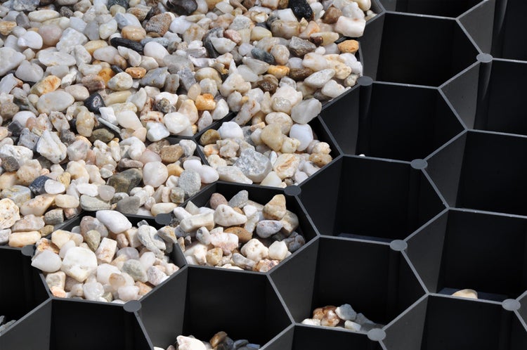 Schwarzes Kiesgitter aus Kunststoff mit Wabenstruktur, teilweise mit hellem Kies befüllt.