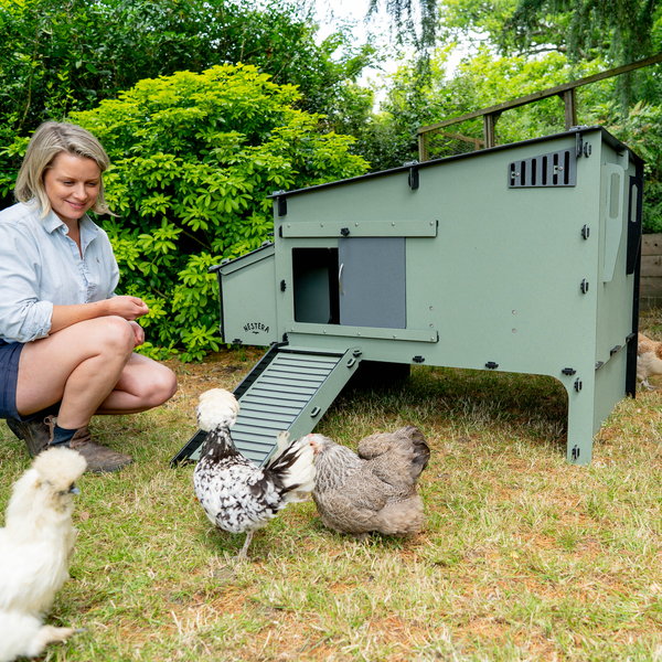 Moderner Nestera Hühnerstall aus recyceltem Kunststoff im Garten mit Hühnern und einer Frau.