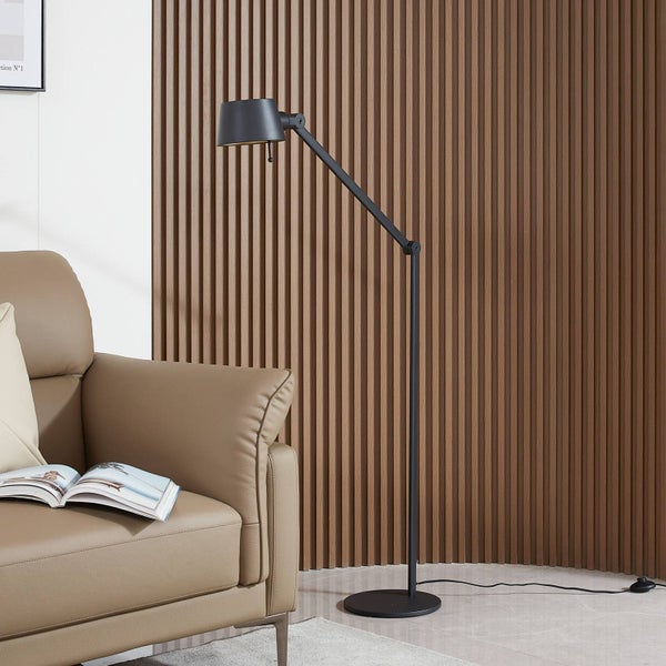 Schwarze Stehleuchte mit verstellbarem Metallarm neben einem Ledersessel vor einer Wand aus Holzlamellen in einem hellen, geordneten Wohnzimmer.