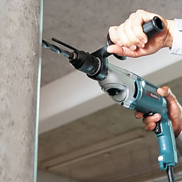 Makita Bohrhammer beim Bohren in eine Betonwand mit Zusatzhandgriff.