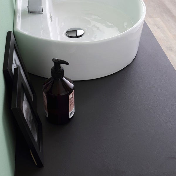 Ovales Aufsatzwaschbecken in Weiß auf einer dunkelgrauen Waschtischplatte in Lederoptik mit Seifenspender und Bilderrahmen.